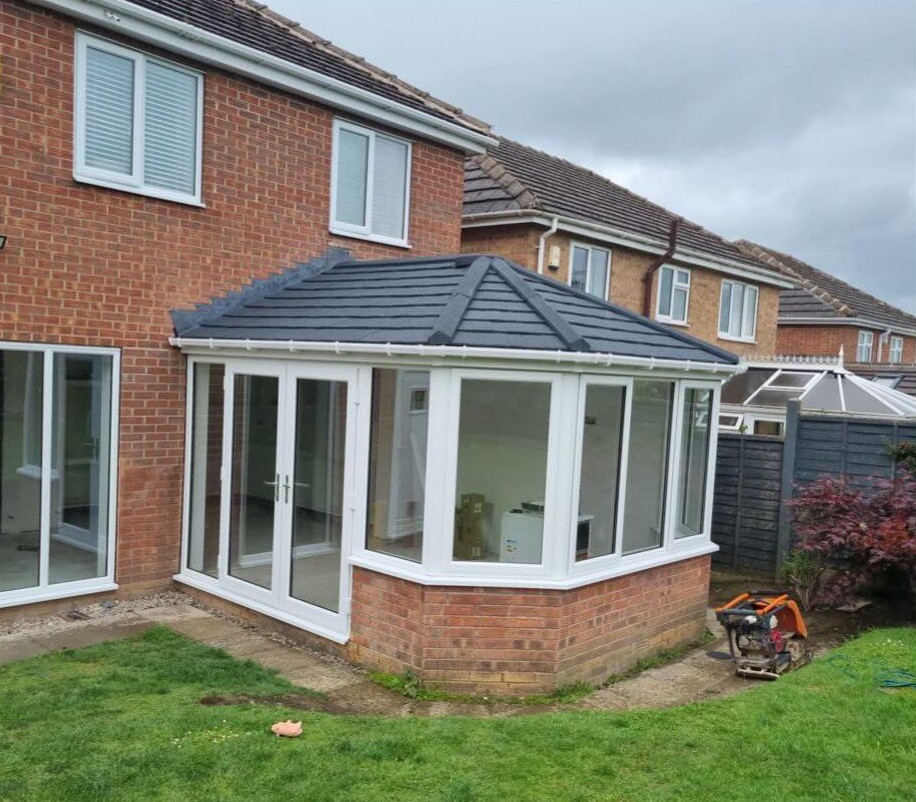 Finished white conservatory with a grey tiled roof, seen from the side