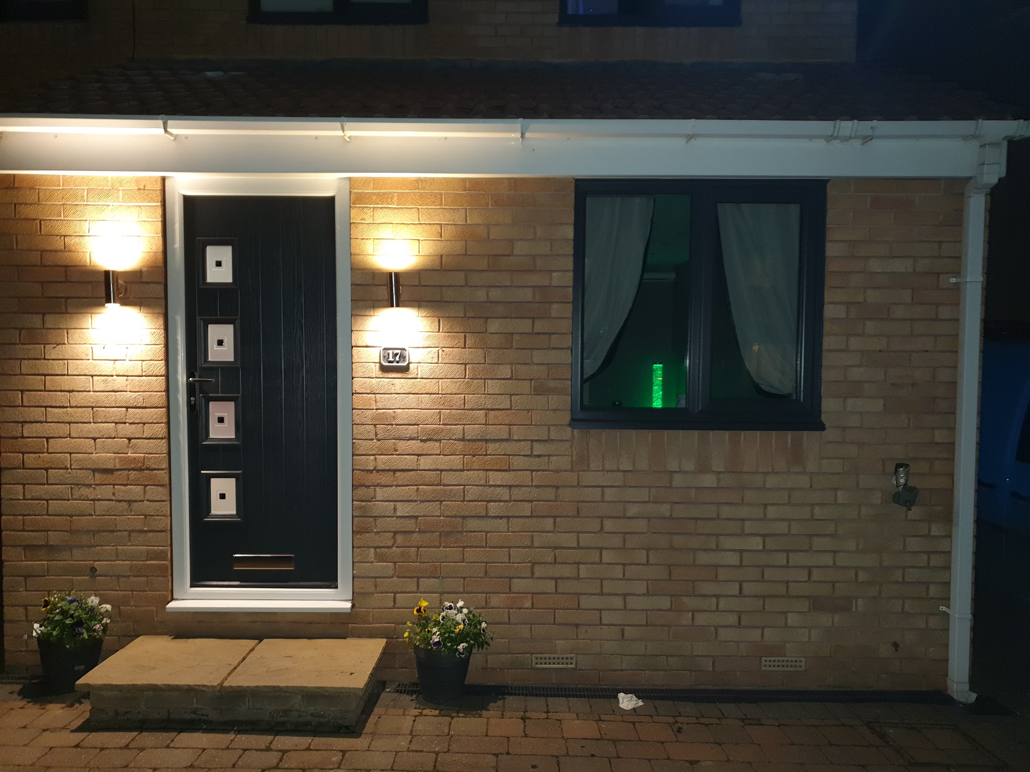 A black composite front door lit up at dusk, with wall lights either side